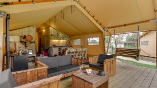 Interieur van het Forest Lodge safaritent bij Sandberghe in Nederland, met zithoek en houten schommelbank.