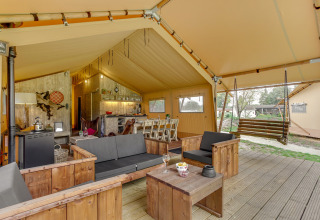 Interior de la tienda safari Forest Lodge en Sandberghe, Países Bajos, con sala y banco colgante de madera.