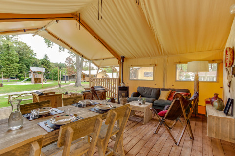 Safari-Zelt Forest Lodge im Sandberghe, Niederlande, mit Holzmöbeln, Essbereich und Blick ins Grüne.