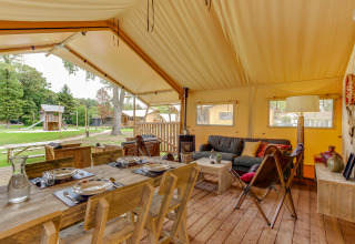 Safari-Zelt Forest Lodge im Sandberghe, Niederlande, mit Holzmöbeln, Essbereich und Blick ins Grüne.