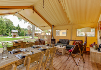 Safari telt Forest Lodge ved Sandberghe i Holland med træmøbler, spisestue og udsigt til legepladsen udenfor.