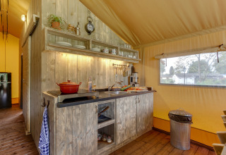 Køkkenområdet i et safaritelt på Forest Lodge, Sandberghe, Holland, med træskabe og vindue.