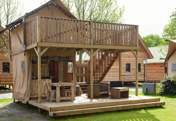Tienda safari Forest Lodge Junior en Sandberghe, Países Bajos, con terraza y balcón de madera al aire libre.