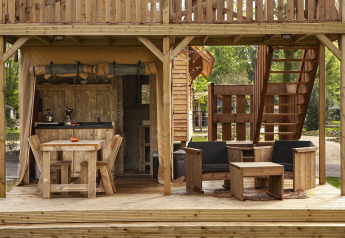 Houten terras met zetels en keuken in de safaritent Forest Lodge Junior bij Sandberghe, Nederland.