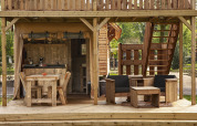 Houten terras met zetels en keuken in de safaritent Forest Lodge Junior bij Sandberghe, Nederland.