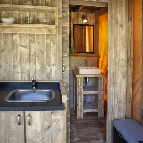 Keuken- en badkamerhoek in het Forest Lodge Junior safaritent bij Sandberghe, Nederland, met houten inrichting.