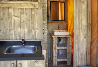 Keuken- en badkamerhoek in het Forest Lodge Junior safaritent bij Sandberghe, Nederland, met houten inrichting.