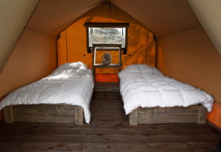 Interior de una tienda safari con dos camas individuales y ropa de cama blanca en Forest Lodge Junior en Sandberghe.