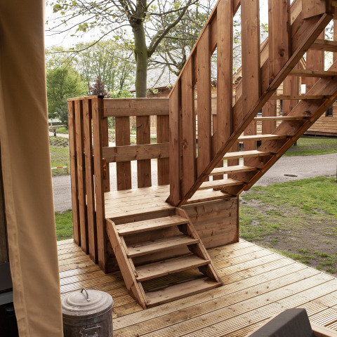 Houten trap en balkon bij een safaritent in Forest Lodge Junior op Sandberghe, Nederland omringd door bomen.