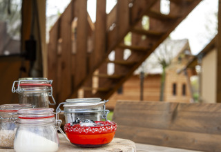 Tarros de cristal y un cuenco rojo sobre una mesa frente a una escalera en la tienda safari Forest Lodge Junior, Sandberghe.