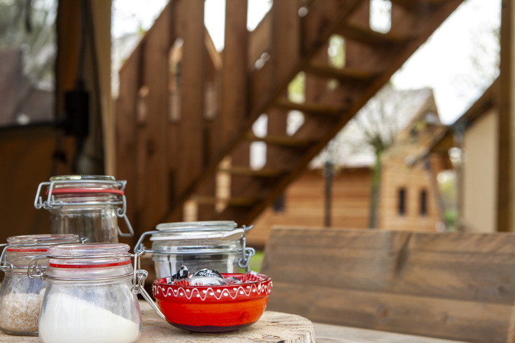 Tarros de cristal y un cuenco rojo sobre una mesa frente a una escalera en la tienda safari Forest Lodge Junior, Sandberghe.