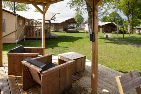 Uitzicht vanaf een overdekt houten terras met stoelen bij Forest Lodge Junior safaritent op Sandberghe, Nederland.