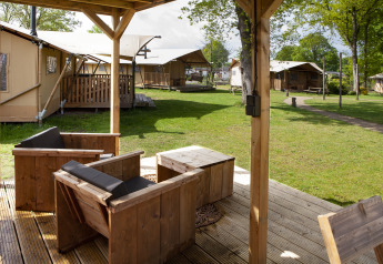 Blick von einer überdachten Terrasse mit Holzmöbeln auf Safarizelte im Forest Lodge Junior in Sandberghe.