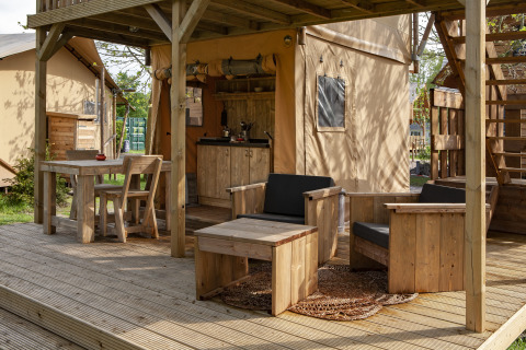 Zona exterior con muebles de madera y cocina en una tienda safari, Forest Lodge Junior en Sandberghe, Países Bajos.