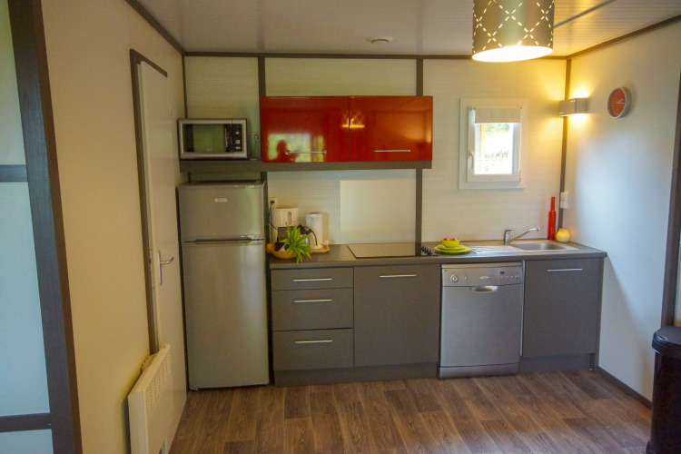 Cocina moderna de una cabaña con armarios grises, electrodomésticos y suelo de madera.