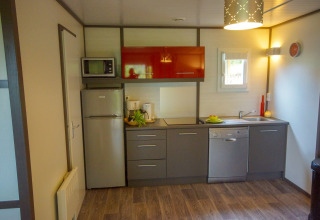 Cocina moderna de una cabaña con armarios grises, electrodomésticos y suelo de madera.