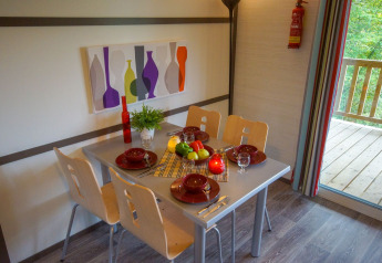 Eettafel gedekt voor vier in een lodge, met fruit, rood servies en schilderij van flessen aan de muur.
