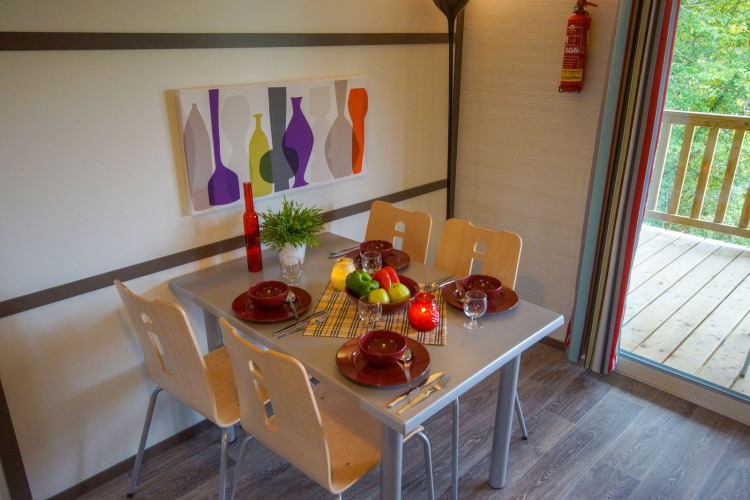 Mesa de comedor para cuatro en una cabaña, con frutero, vajilla roja y pintura colorida de botellas en la pared.