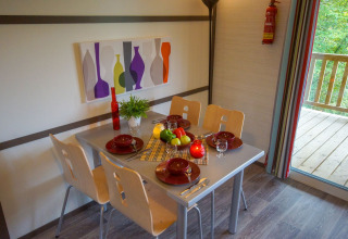 Mesa de comedor para cuatro en una cabaña, con frutero, vajilla roja y pintura colorida de botellas en la pared.