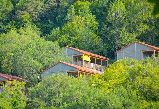 Cabañas de madera con techos rojos entre frondosos árboles verdes, parte de un lodge en la montaña.