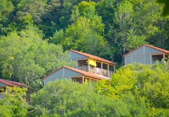 Træhytter med røde tage ligger blandt grønne træer på en bakke ved en lodge, badet i sollys.