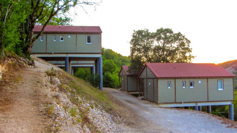 Cabañas con techos rojos sobre pilotes en Chalet Belvedere, La Draille, Francia, rodeadas de bosque y colinas.