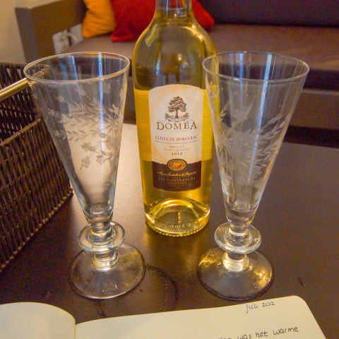 Dos copas de vino y una botella de vino Doméa sobre una mesa en un lodge, con un diario al frente.