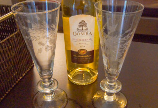 Dos copas de vino y una botella de vino Doméa sobre una mesa en un lodge, con un diario al frente.