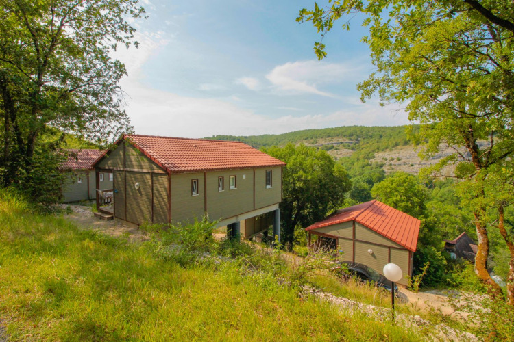Photo of a lodge with red roofs nestled among green trees and rolling hills under a bright blue sky.