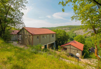 Foto di un lodge dai tetti rossi immerso tra alberi verdi e colline sotto un cielo sereno e limpido.