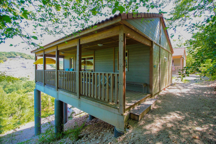 A charming wooden lodge on stilts with a covered porch, nestled among trees in a peaceful natural setting.
