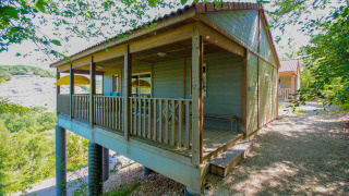 Acogedora cabaña de madera sobre pilotes con porche cubierto, rodeada de árboles y naturaleza tranquila.
