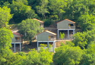 Cuatro cabañas de madera elevadas con techos rojos en Chalet Belvedere, La Draille, rodeadas de bosque en Francia.