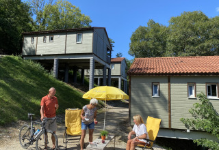 Tres adultos y una bicicleta junto a sillas amarillas en Chalet Belvedere en La Draille, Francia, bajo el sol.