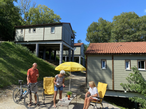 Tres adultos y una bicicleta junto a sillas amarillas en Chalet Belvedere en La Draille, Francia, bajo el sol.