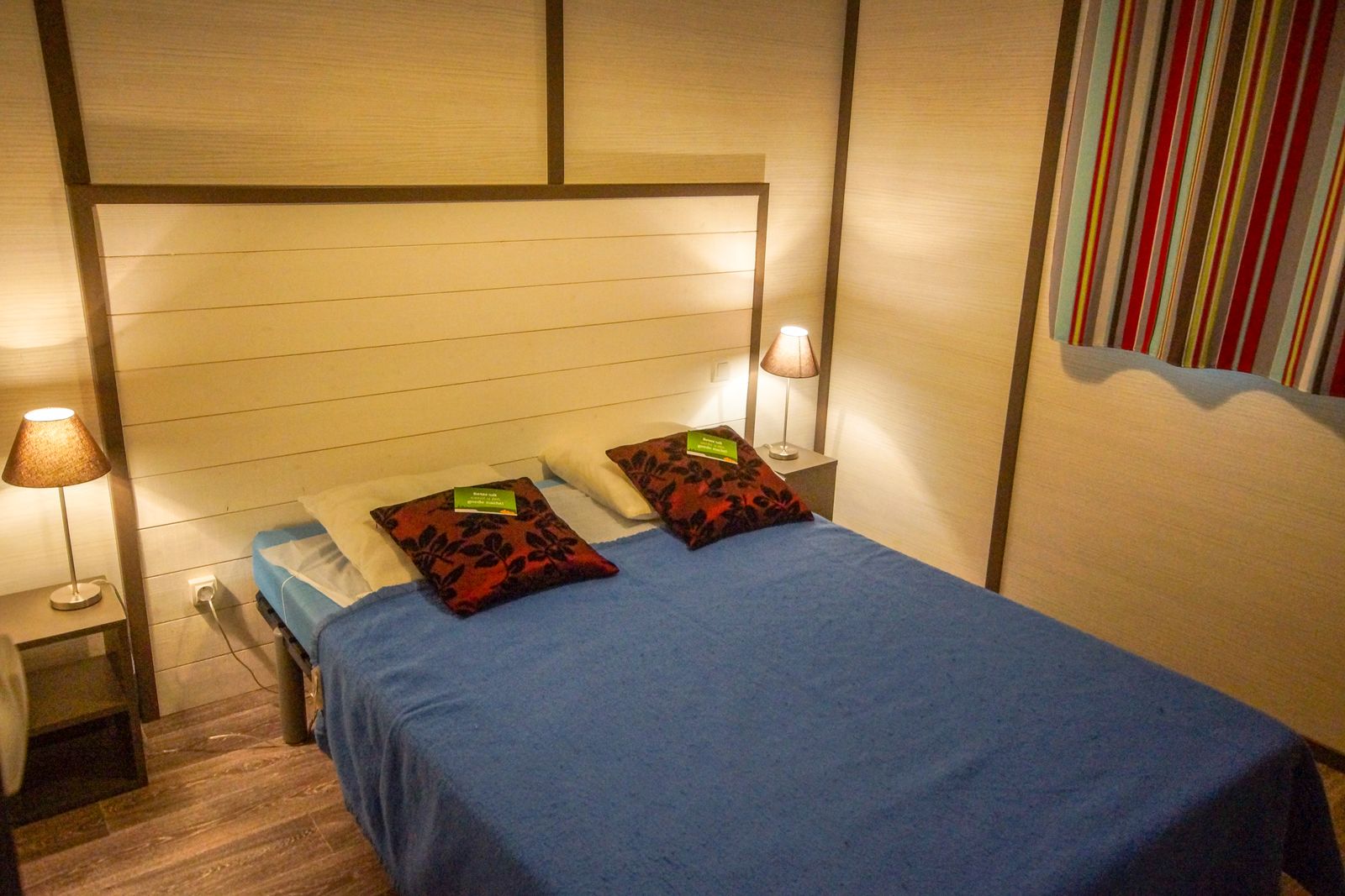 Slaapkamer in Chalet Belvedere Deluxe in La Draille, Frankrijk met tweepersoonsbed, lampen en kleurrijk gordijn.