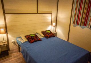 Dormitorio en Chalet Belvedere Deluxe en La Draille, Francia con cama doble, lámparas y cortina colorida.