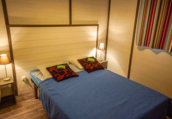 Soveværelse på Chalet Belvedere Deluxe i La Draille, Frankrig med dobbeltseng, lamper og farverigt gardin.