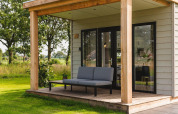 Tiny house med hyggelig overdækket veranda, grå sofa og grønne omgivelser i et fredeligt landskab.
