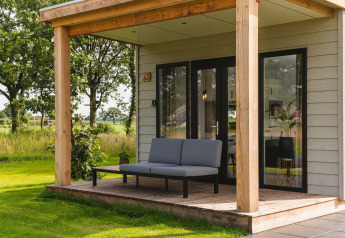 Tiny house con veranda coperta, moderno divano grigio e vista verde su un tranquillo paesaggio rurale.