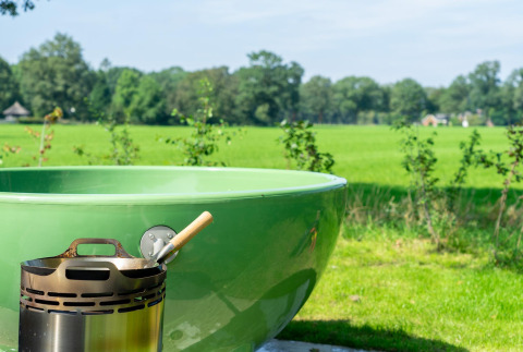 Green outdoor tub and fire pit with pan in front of fields at Vakantiepark Hölte, Netherlands panorama lodge.