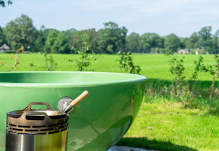 Grüne Außendusche und Feuerstelle mit Pfanne vor Aussicht auf Felder im Vakantiepark Hölte, Niederlande.