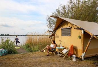 Donna che si rilassa davanti a una tenda safari presso il lago, mentre un'altra fa yoga a Marina Parcs Almere, Paesi Bassi.