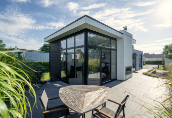 Modern Cube Exclusif 4 lodge at Schoneveld, Netherlands featuring large windows, terrace, and sunny garden.