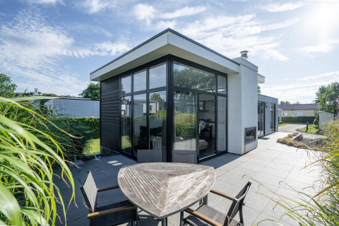 Lodge Cube Exclusif 4 moderne à Schoneveld, Pays-Bas, grandes fenêtres, terrasse et espace extérieur ensoleillé.