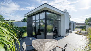 Lodge Cube Exclusif 4 moderne à Schoneveld, Pays-Bas, grandes fenêtres, terrasse et espace extérieur ensoleillé.
