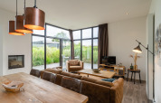 Salon moderne du lodge Cube Exclusif 4 à Schoneveld, Pays-Bas, avec grandes fenêtres et décoration chaleureuse.