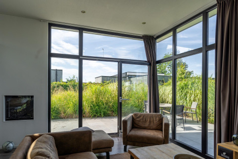 Living room in Cube Exclusif 4 lodge at Schoneveld, Netherlands, featuring large windows and patio view.