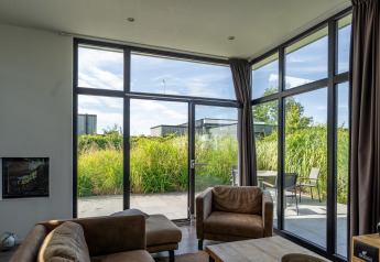 Living room in Cube Exclusif 4 lodge at Schoneveld, Netherlands, featuring large windows and patio view.