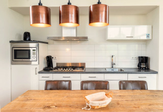 Moderne Küche in der Cube Exclusif 4 Lodge in Schoneveld, Niederlande, mit Holz­tisch und Kupferlampen.